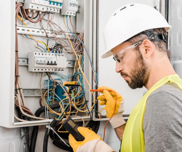 handsome electrician checking electrical box with multimetr in corridor